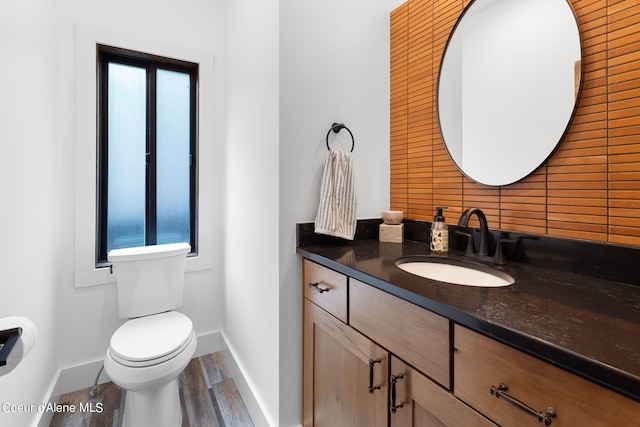 half bathroom with vanity, baseboards, toilet, and wood finished floors