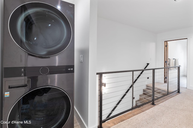 laundry room featuring stacked washing maching and dryer, wood finished floors, laundry area, and baseboards