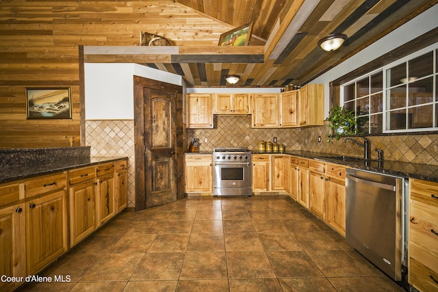 kitchen featuring wooden walls, dark tile patterned floors, a sink, appliances with stainless steel finishes, and backsplash