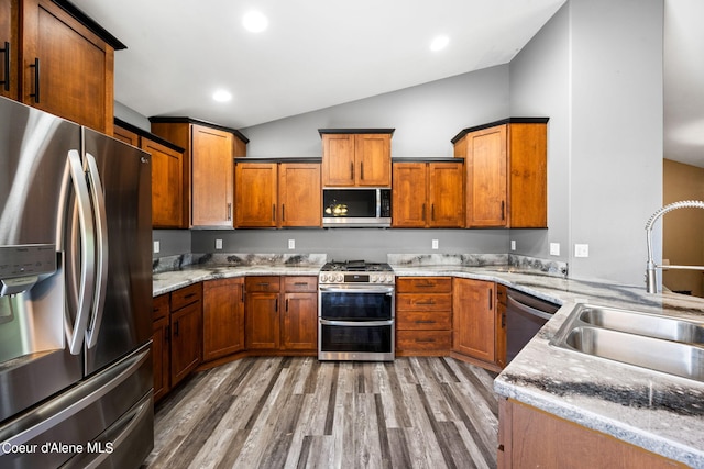 kitchen with brown cabinetry, lofted ceiling, light wood-style floors, a sink, and stainless steel appliances