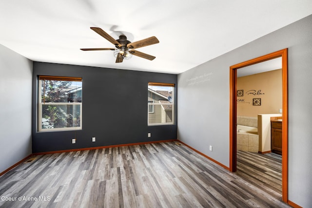 unfurnished bedroom featuring connected bathroom, baseboards, multiple windows, and wood finished floors