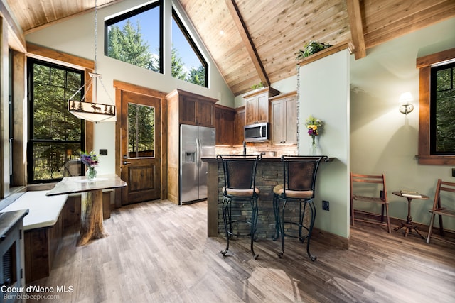 kitchen with appliances with stainless steel finishes, wood ceiling, light hardwood / wood-style floors, and a kitchen breakfast bar