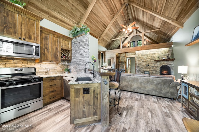 kitchen featuring sink, a stone fireplace, kitchen peninsula, high vaulted ceiling, and appliances with stainless steel finishes