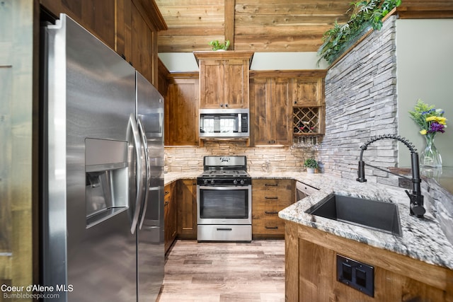 kitchen with stainless steel appliances, light stone countertops, light hardwood / wood-style flooring, and sink