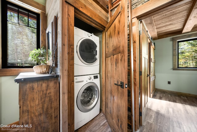 washroom featuring stacked washer / dryer, a barn door, wooden ceiling, and wood-type flooring