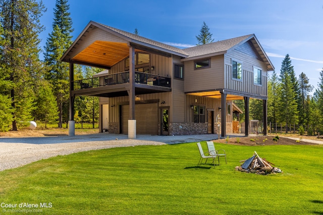 rear view of property with a balcony, a garage, a lawn, and an outdoor fire pit