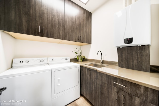 clothes washing area with cabinets, sink, washing machine and dryer, and water heater