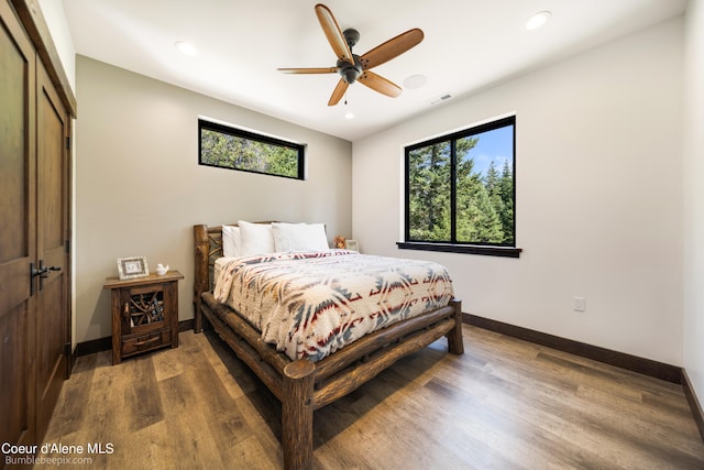 bedroom with multiple windows, ceiling fan, dark wood-type flooring, and a closet