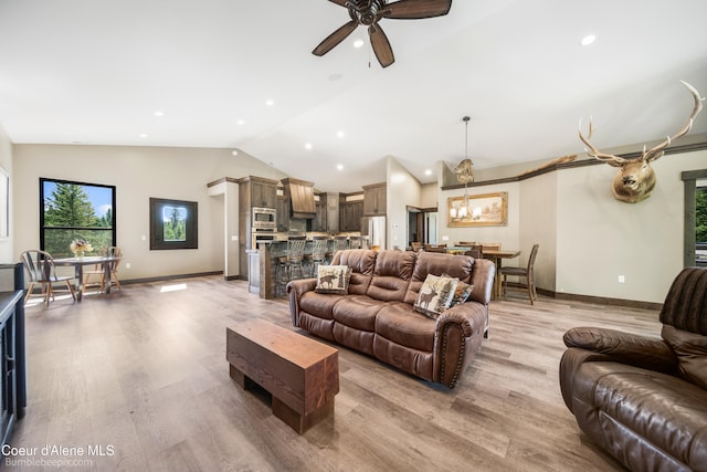 living room featuring ceiling fan with notable chandelier, vaulted ceiling, and light hardwood / wood-style floors