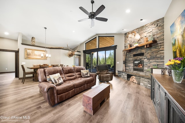 living room featuring ceiling fan with notable chandelier, light wood-type flooring, a fireplace, and high vaulted ceiling