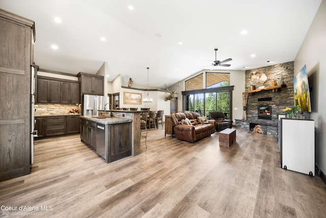 kitchen with ceiling fan, dark brown cabinetry, a stone fireplace, a center island with sink, and light hardwood / wood-style flooring