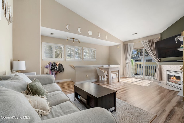 living room with high vaulted ceiling, a healthy amount of sunlight, a premium fireplace, and light wood-type flooring