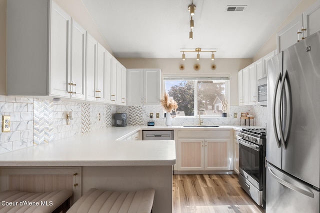 kitchen featuring tasteful backsplash, appliances with stainless steel finishes, kitchen peninsula, white cabinetry, and light hardwood / wood-style flooring