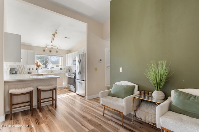 kitchen with white cabinets, decorative backsplash, appliances with stainless steel finishes, a breakfast bar, and light hardwood / wood-style floors