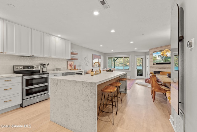 kitchen featuring white cabinets, a center island with sink, and double oven range