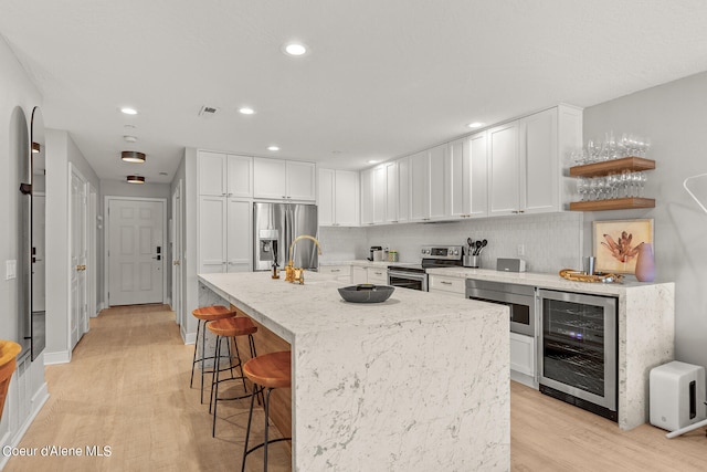 kitchen featuring white cabinets, wine cooler, appliances with stainless steel finishes, a breakfast bar area, and light wood-type flooring