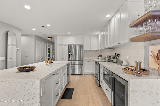 kitchen featuring beverage cooler, light hardwood / wood-style flooring, stainless steel appliances, light stone countertops, and white cabinets