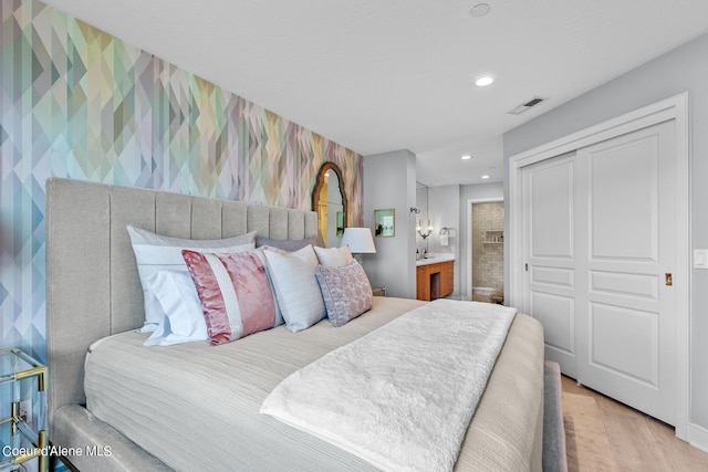 bedroom featuring a closet, ensuite bath, and light hardwood / wood-style flooring