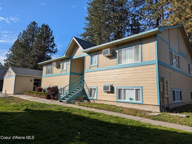 view of front of house with a wall mounted air conditioner and a front yard