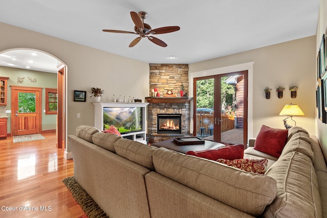 living room featuring ceiling fan, light hardwood / wood-style flooring, and a stone fireplace