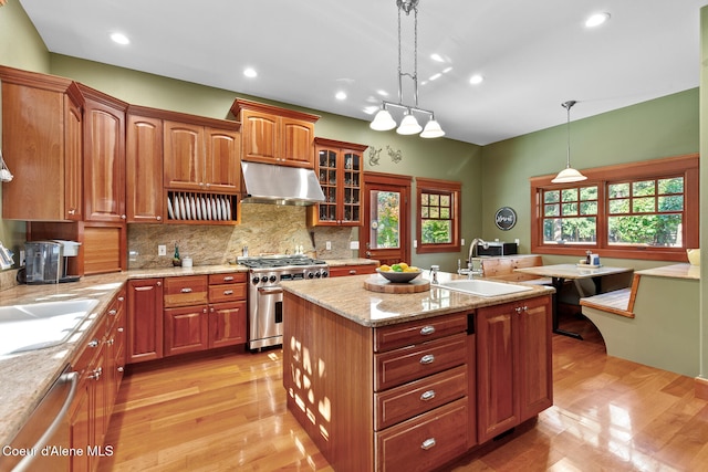 kitchen featuring appliances with stainless steel finishes, light wood-type flooring, hanging light fixtures, and a center island with sink