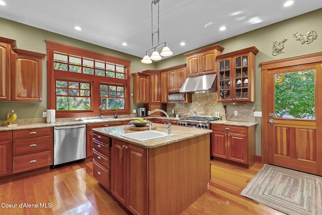 kitchen featuring light stone counters, stainless steel appliances, light hardwood / wood-style floors, a center island with sink, and decorative light fixtures