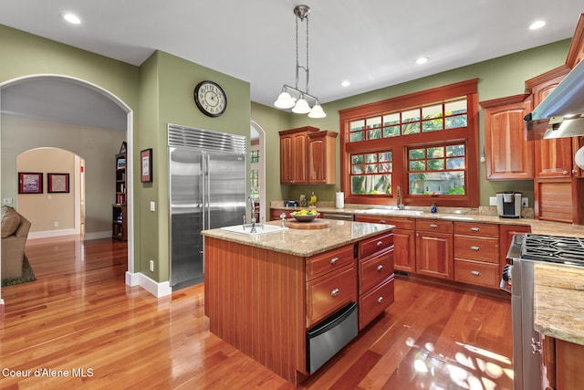 kitchen featuring wood-type flooring, a center island with sink, decorative light fixtures, sink, and appliances with stainless steel finishes