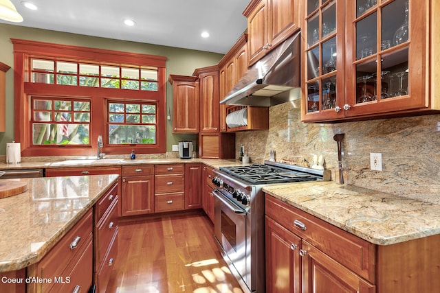 kitchen featuring light stone countertops, tasteful backsplash, high end stainless steel range oven, sink, and light hardwood / wood-style flooring