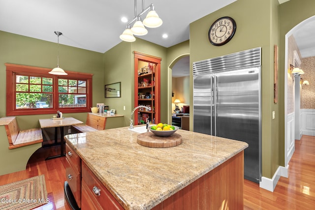 kitchen with stainless steel built in refrigerator, a center island with sink, and pendant lighting