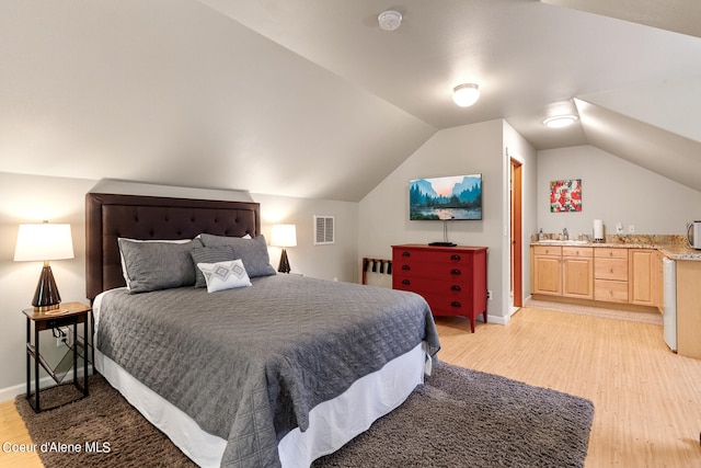 bedroom with sink, light hardwood / wood-style floors, ensuite bath, and vaulted ceiling