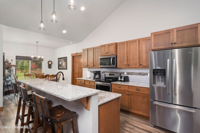 kitchen featuring decorative light fixtures, decorative backsplash, a kitchen island with sink, appliances with stainless steel finishes, and a kitchen breakfast bar