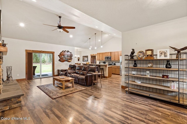 living room with hardwood / wood-style flooring, ceiling fan, high vaulted ceiling, and a stone fireplace