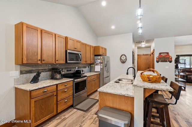 kitchen featuring an island with sink, appliances with stainless steel finishes, decorative light fixtures, light stone counters, and sink