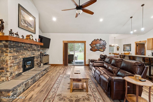 living room with a fireplace, lofted ceiling, light hardwood / wood-style floors, and ceiling fan with notable chandelier