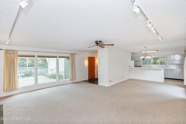 unfurnished living room with track lighting, ceiling fan with notable chandelier, light colored carpet, and a textured ceiling