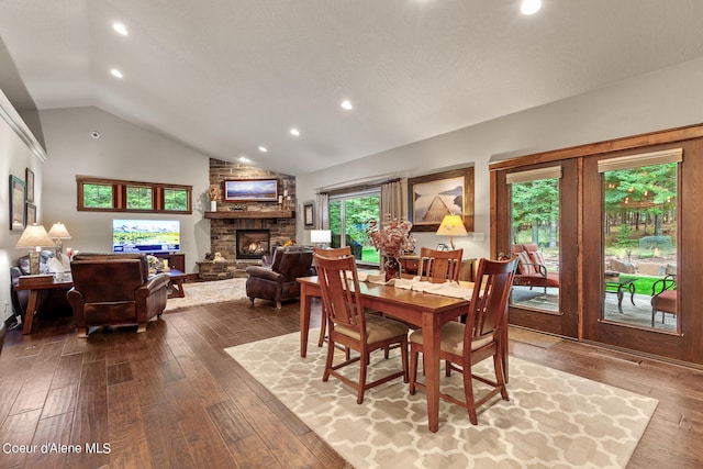 dining space with high vaulted ceiling, a stone fireplace, and hardwood / wood-style floors