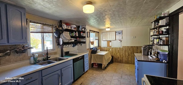 kitchen featuring black range, blue cabinetry, sink, wooden walls, and dishwasher