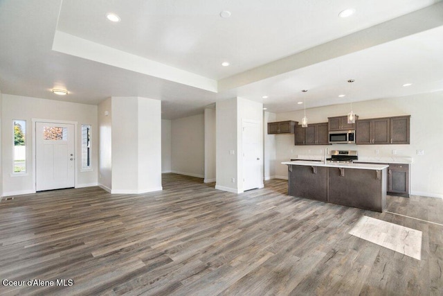 kitchen with appliances with stainless steel finishes, decorative light fixtures, dark hardwood / wood-style floors, and an island with sink