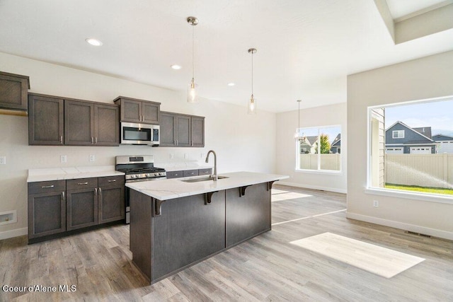 kitchen featuring appliances with stainless steel finishes, sink, light hardwood / wood-style floors, pendant lighting, and a center island with sink