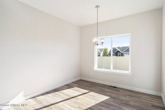 unfurnished room featuring an inviting chandelier and dark hardwood / wood-style flooring