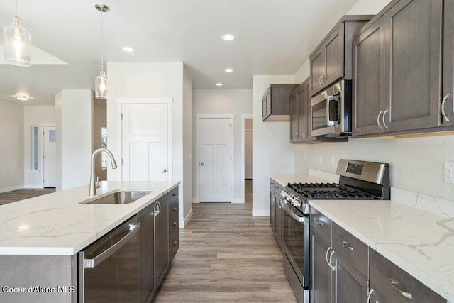 kitchen with light hardwood / wood-style floors, stainless steel appliances, sink, and pendant lighting