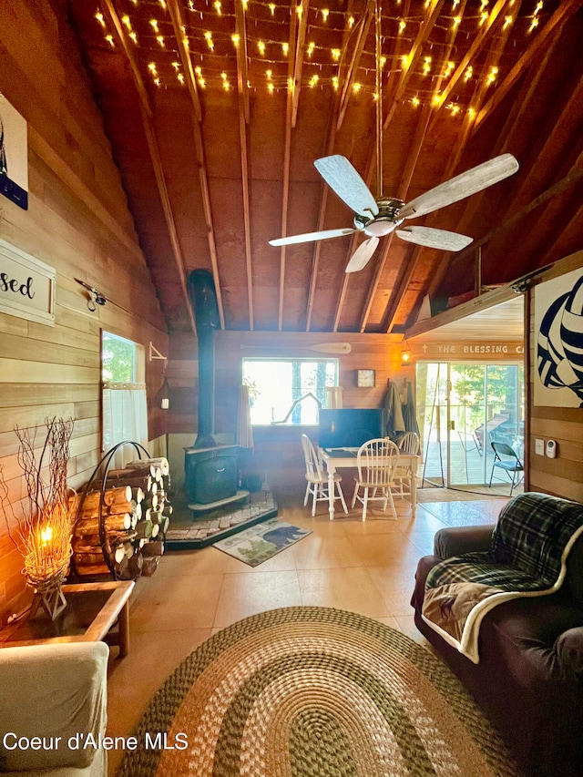 living room with wood walls, a wood stove, ceiling fan, tile patterned floors, and vaulted ceiling