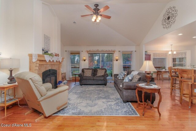 living room with ceiling fan with notable chandelier, high vaulted ceiling, hardwood / wood-style flooring, and a fireplace