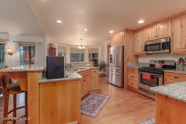 kitchen featuring appliances with stainless steel finishes, light hardwood / wood-style flooring, decorative light fixtures, and light brown cabinetry