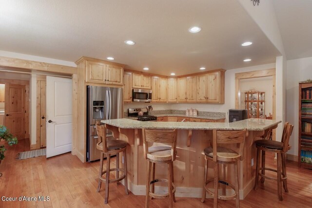 kitchen featuring appliances with stainless steel finishes, light stone countertops, light wood-type flooring, and a breakfast bar area