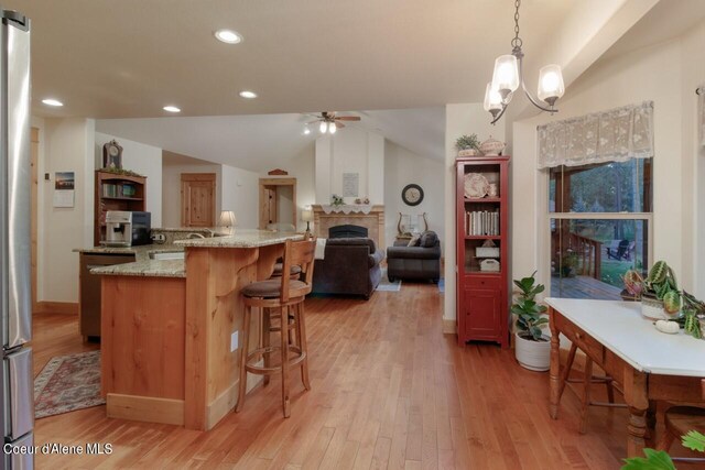 kitchen with lofted ceiling, hanging light fixtures, light stone countertops, light wood-type flooring, and ceiling fan with notable chandelier