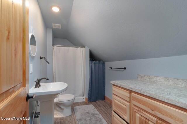 bathroom featuring lofted ceiling, hardwood / wood-style floors, toilet, and walk in shower