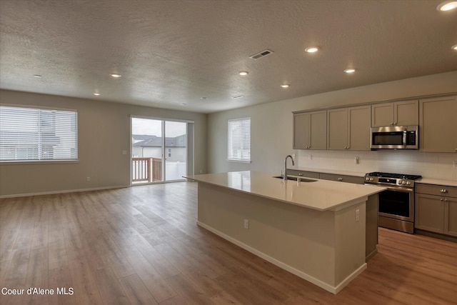 kitchen featuring appliances with stainless steel finishes, sink, an island with sink, backsplash, and light hardwood / wood-style flooring