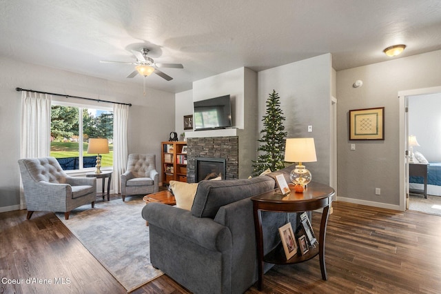 living room with ceiling fan, a stone fireplace, a textured ceiling, and dark hardwood / wood-style flooring