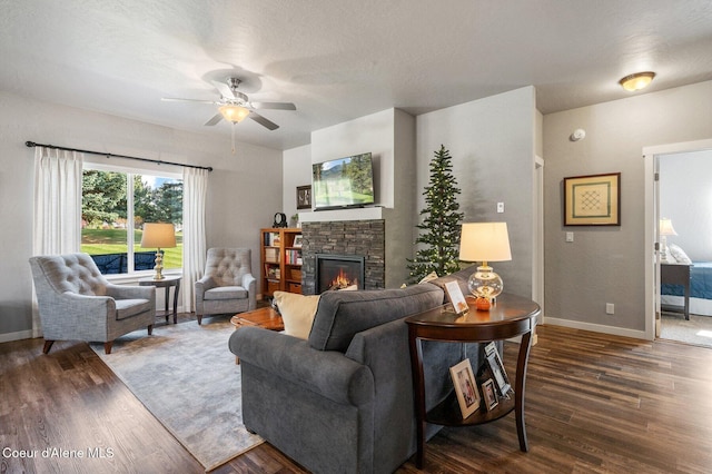 living room with ceiling fan, a stone fireplace, a textured ceiling, and dark hardwood / wood-style floors